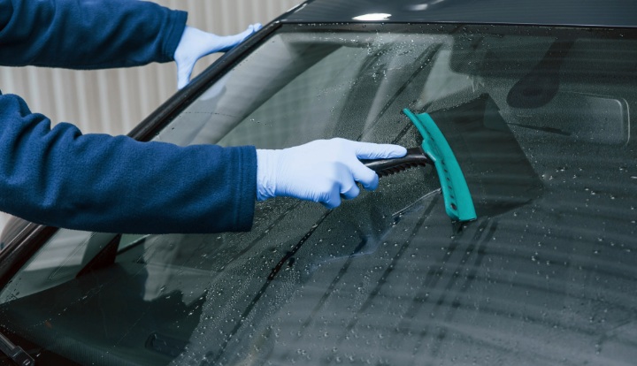 Technician in gloves cleaning car windshield with squeegee during window tint prep