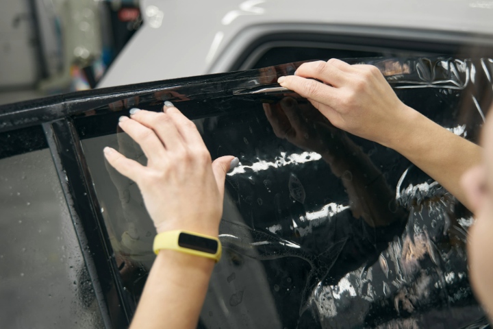 Close-up of hands applying and trimming window tint film on car door