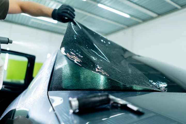Installer applying dark window tint film to car rear windshield with spray bottle and tools